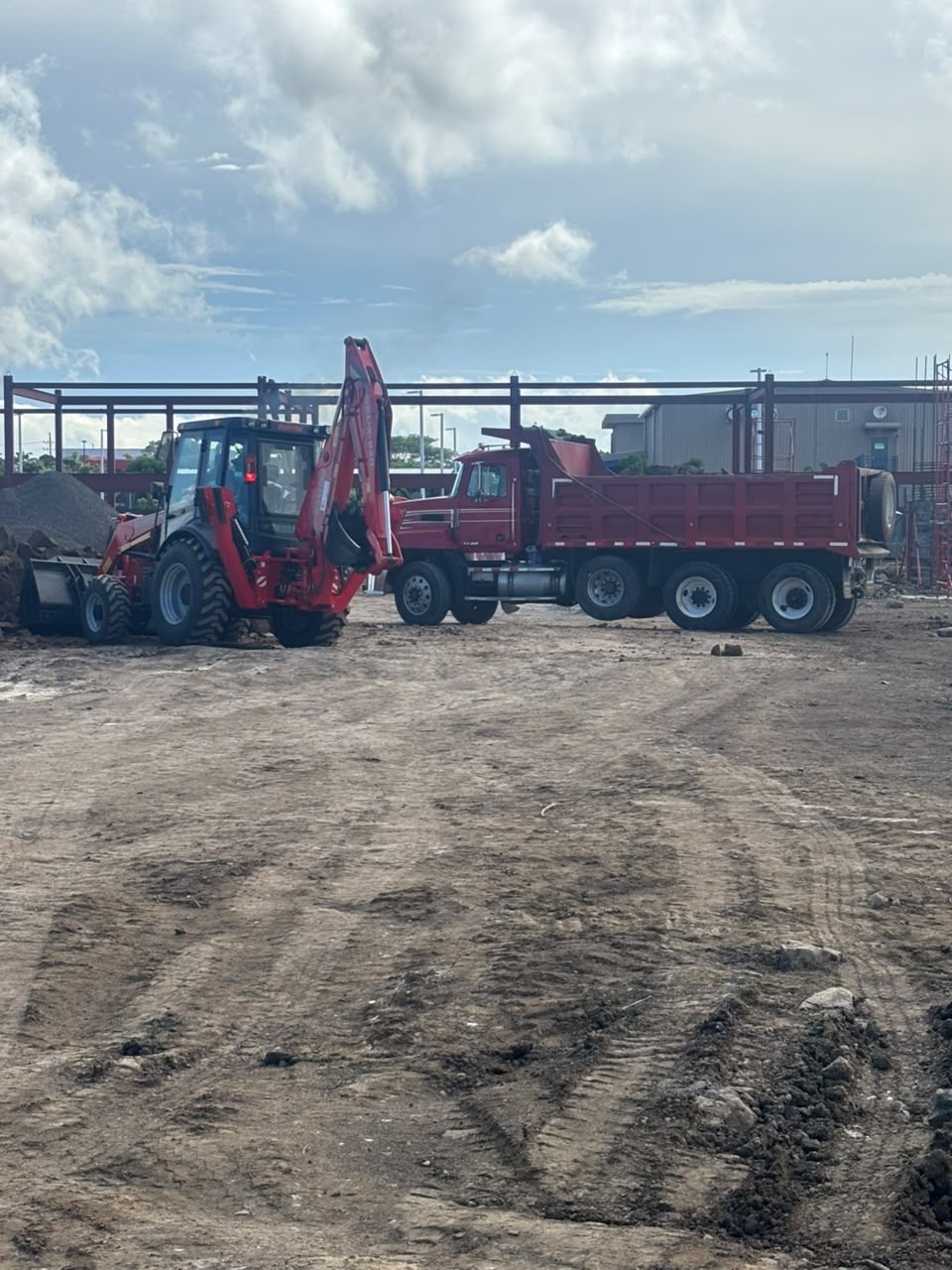 Retroexcavadora roja y vagoneta Mack trabajando en movimiento de tierra
