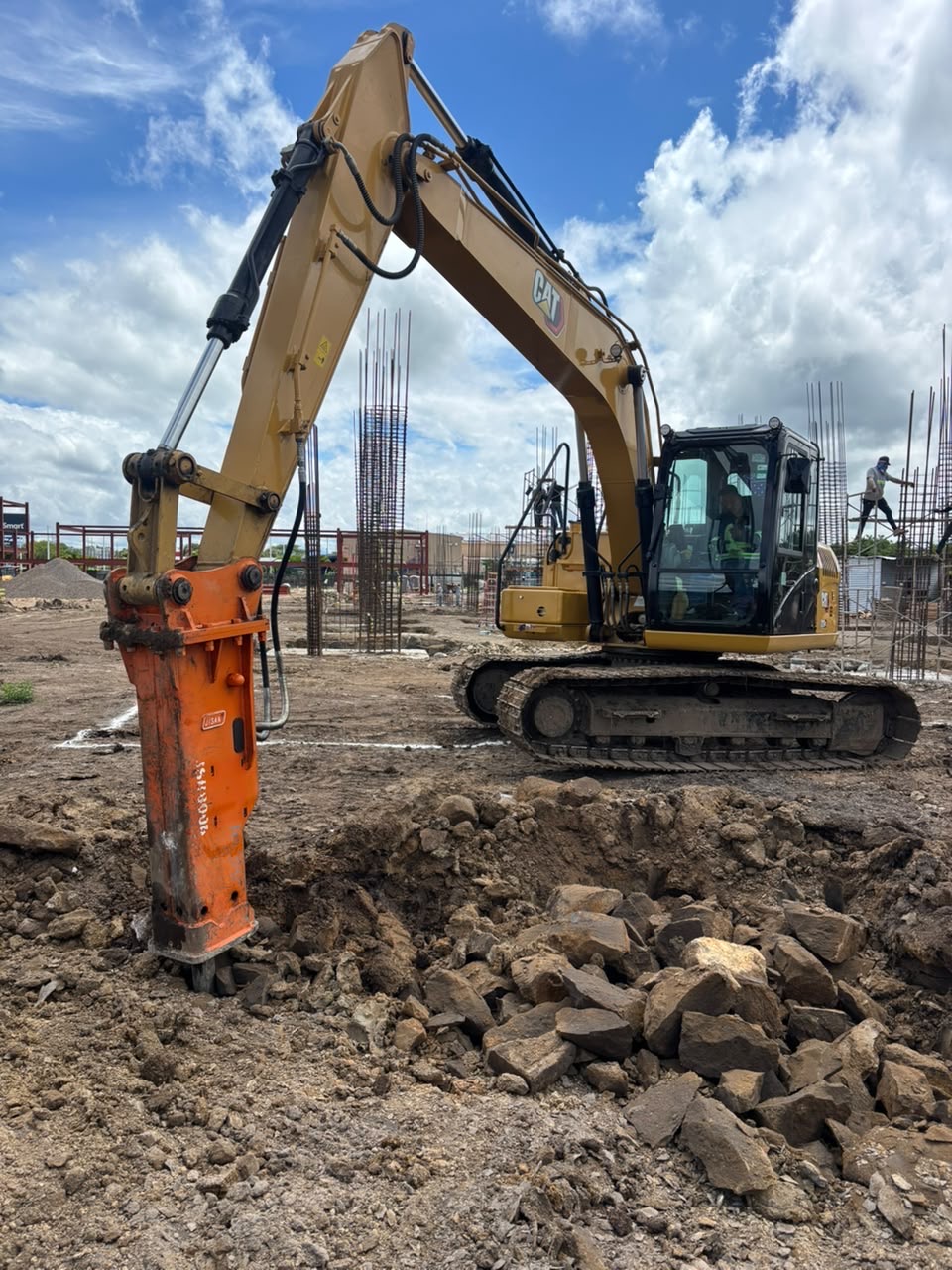 Excavadora CAT con martillo hidráulico en obra con estructura de acero