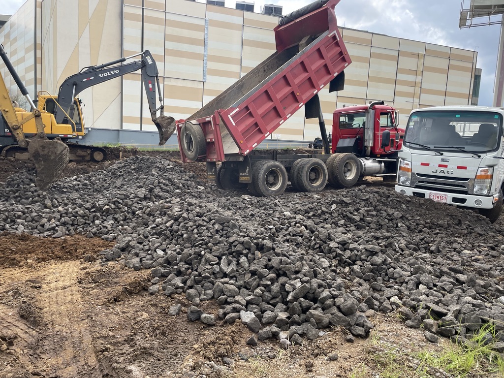 Vagoneta roja SKY descargando agregados junto a excavadora en obra de construcción en Costa Rica